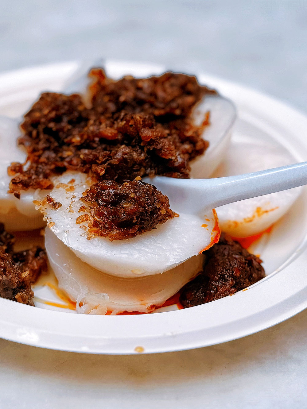 jian-bo-tiong-bahru-chwee-kueh-review Close up Photo of Jian Bo Shui Kueh (Chwee Kueh) on a plate, with a spoon cutting the rice cake